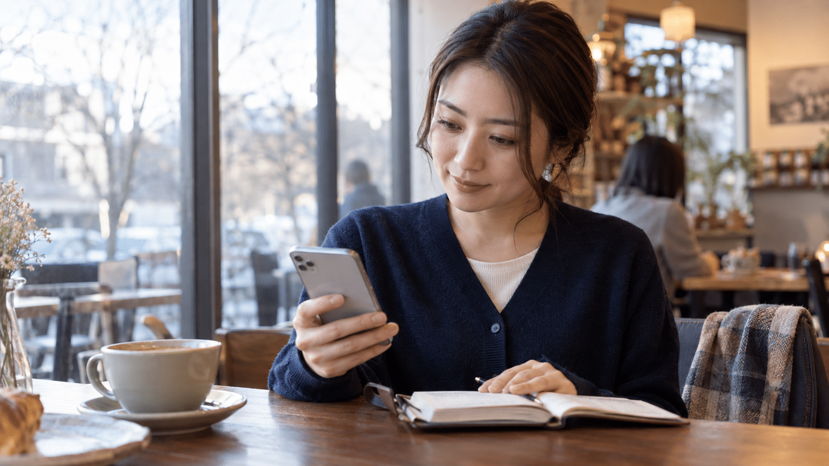 カフェでスマートフォンと手帳を見ながら次の行動を考える女性